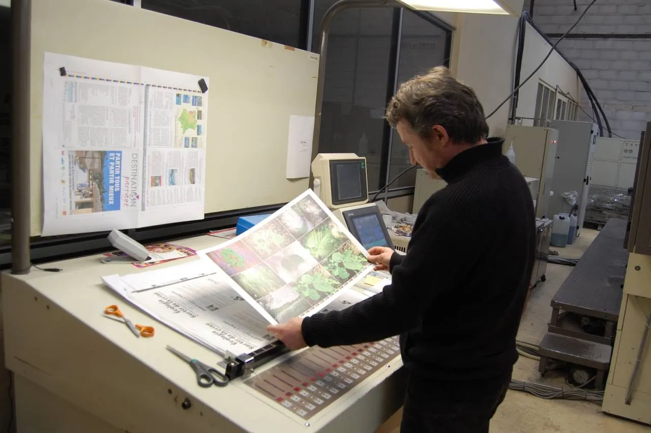 À l'atelier, un imprimeur contrôle une feuille imprimée au pupitre de la presse